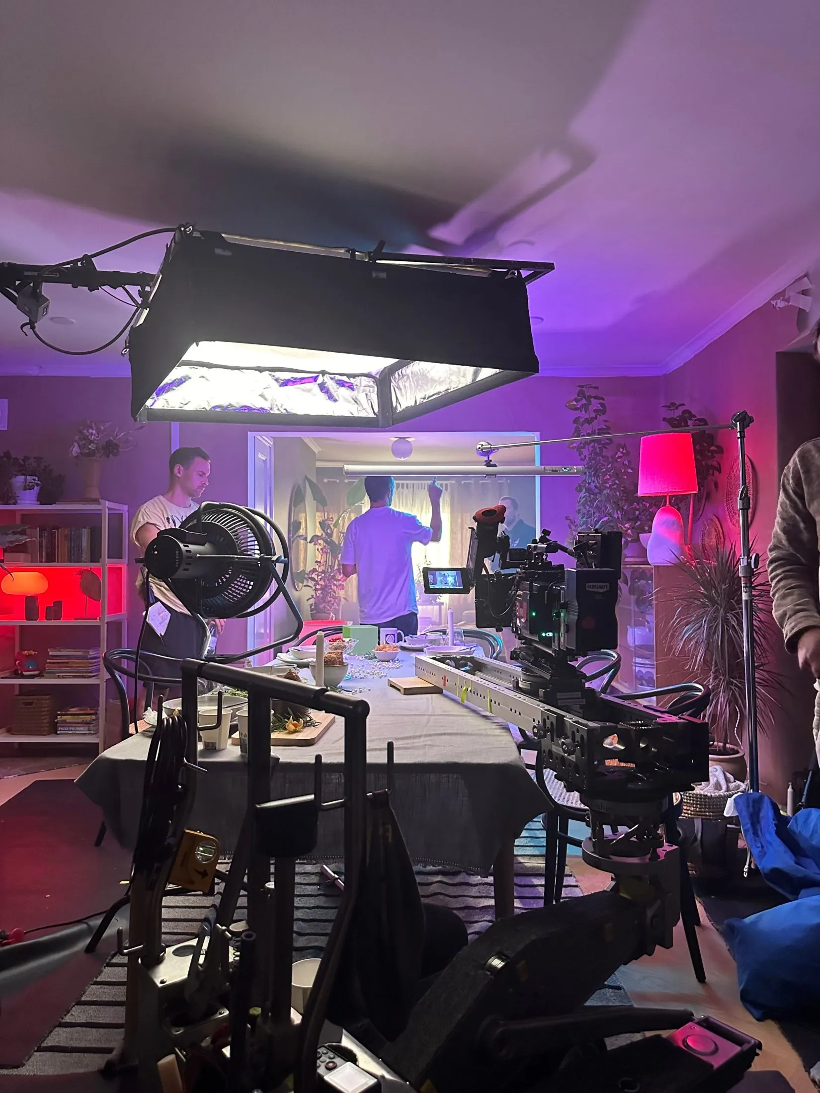 Camera, lighting and crew on an interior set lit in purple.
