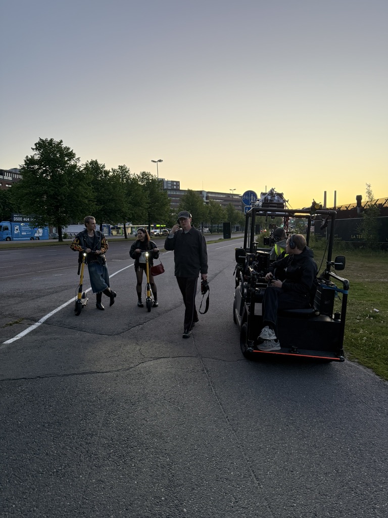 Kuvausryhmä ja kaksi sähköpotkulautaa ilta-auringossa kadulla.