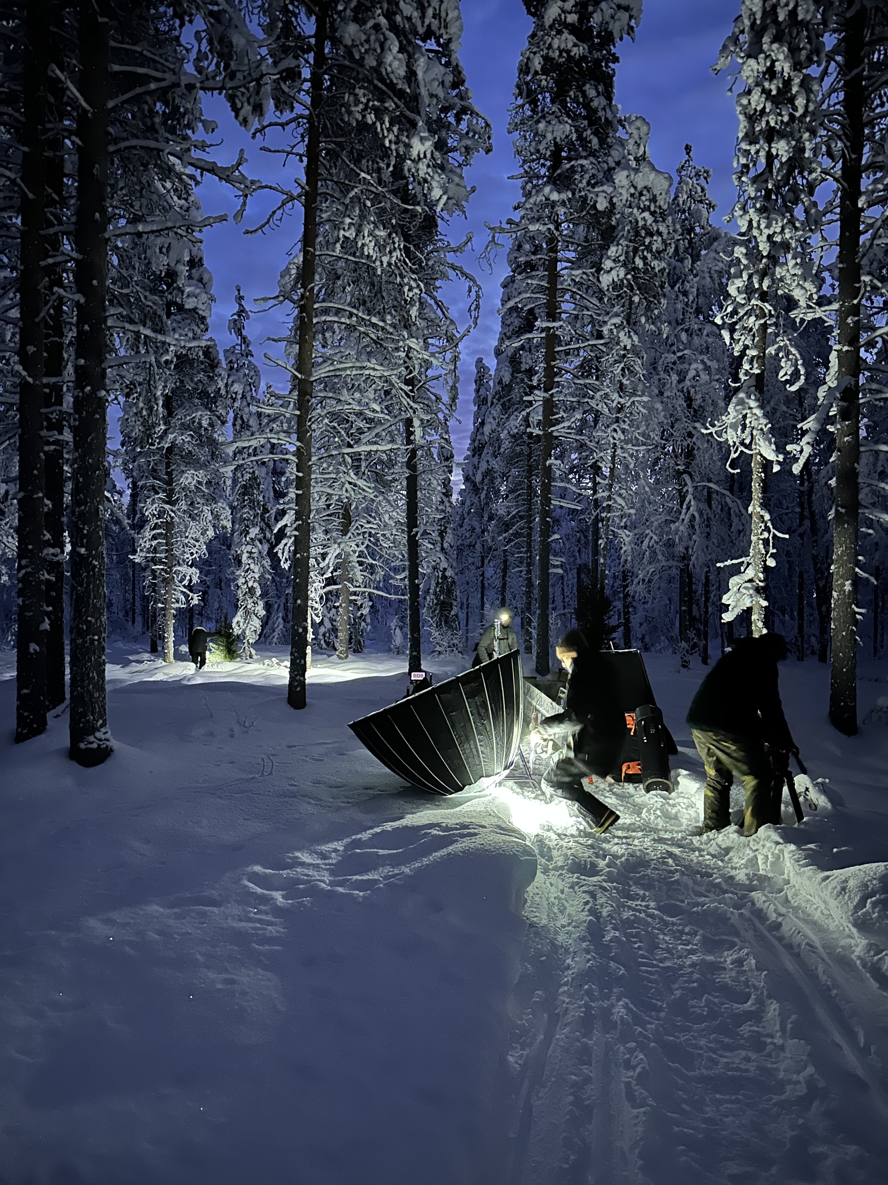Kuvausryhmä ja valokalusto lumisessa metsässä hämärän aikaan S-marketin kuvauksissa.
