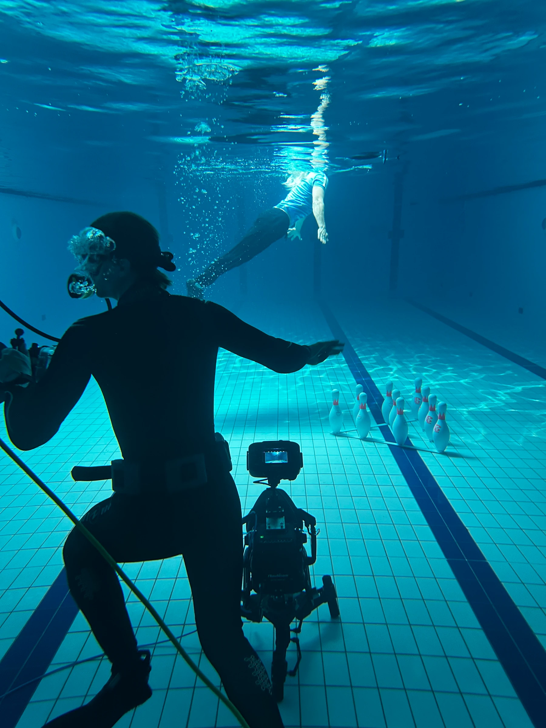 Underwater camera and diver in a swimming pool in front of bowling pins.