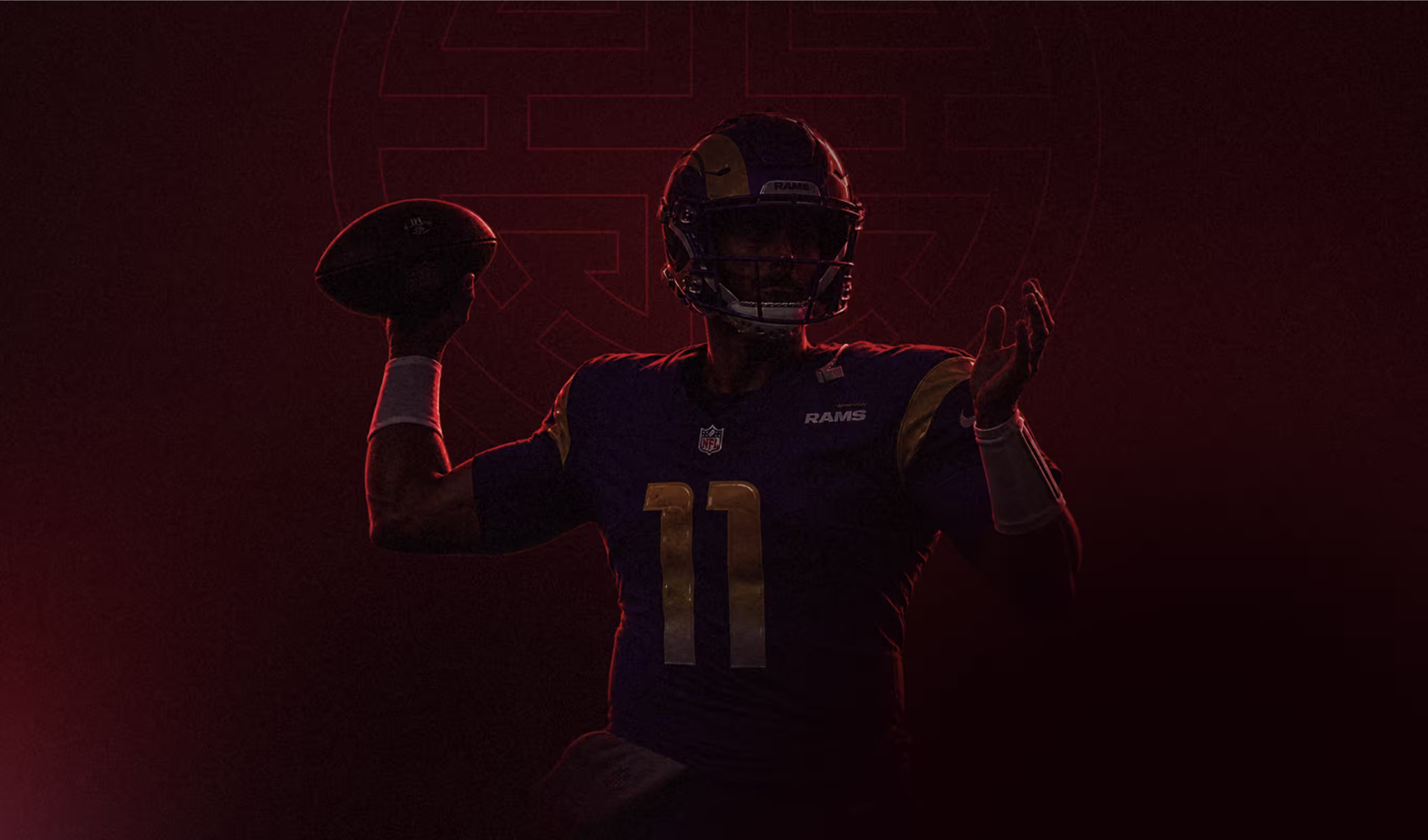 American football player in dark Rams uniform preparing to throw a football at night.