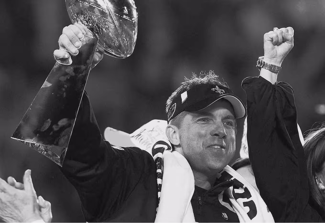 Man wearing a cap and scarf raising a championship trophy and fist in celebration.