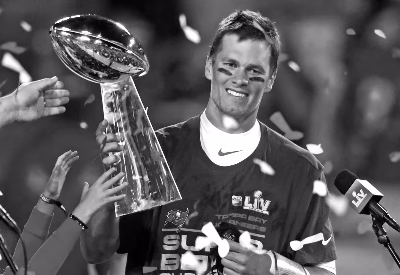 Smiling football player holding the Vince Lombardi Trophy with confetti falling around.