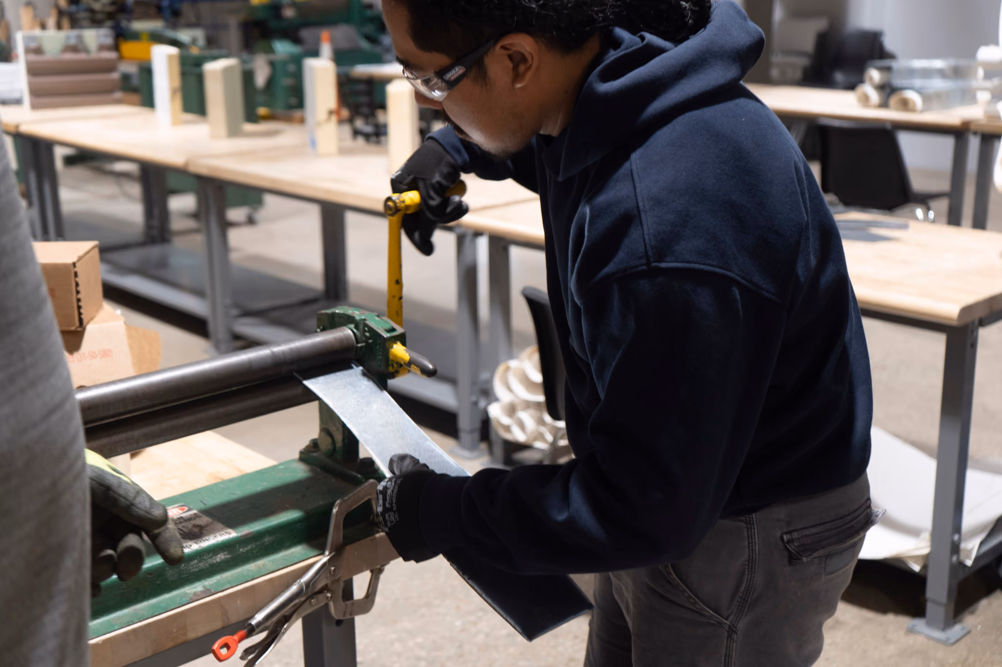 Person in safety glasses and gloves using a metal bending brake in a workshop.