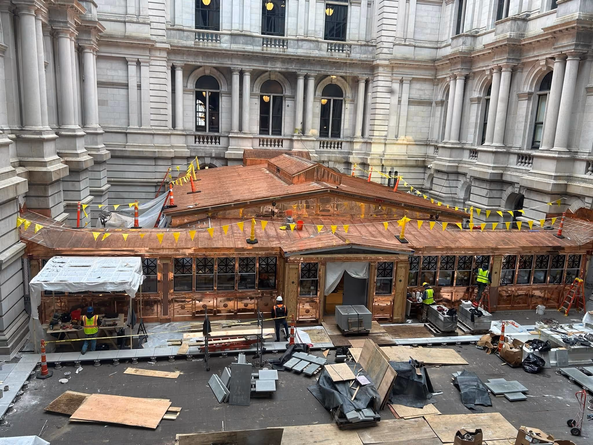 Workers renovating a large copper roof inside a building courtyard, surrounded by stone walls and windows.
