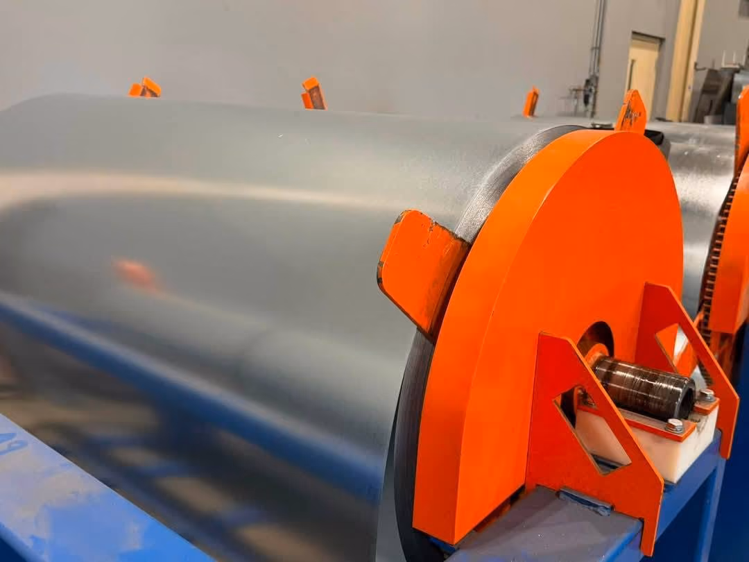 Large rolled sheet metal with bright orange end caps in an industrial setting.