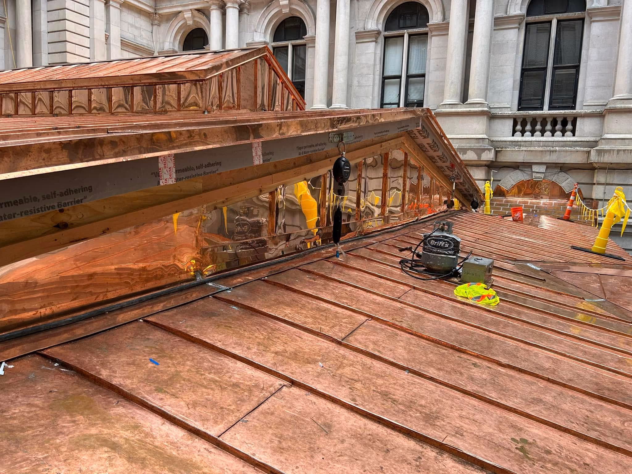 New shiny copper roof panels installed on building under construction with equipment on the roof.