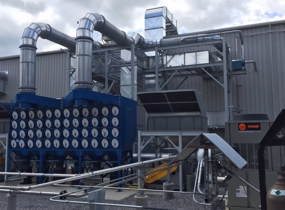 Industrial air filtration and ductwork system with large blue filter housing and metal pipes outside building.