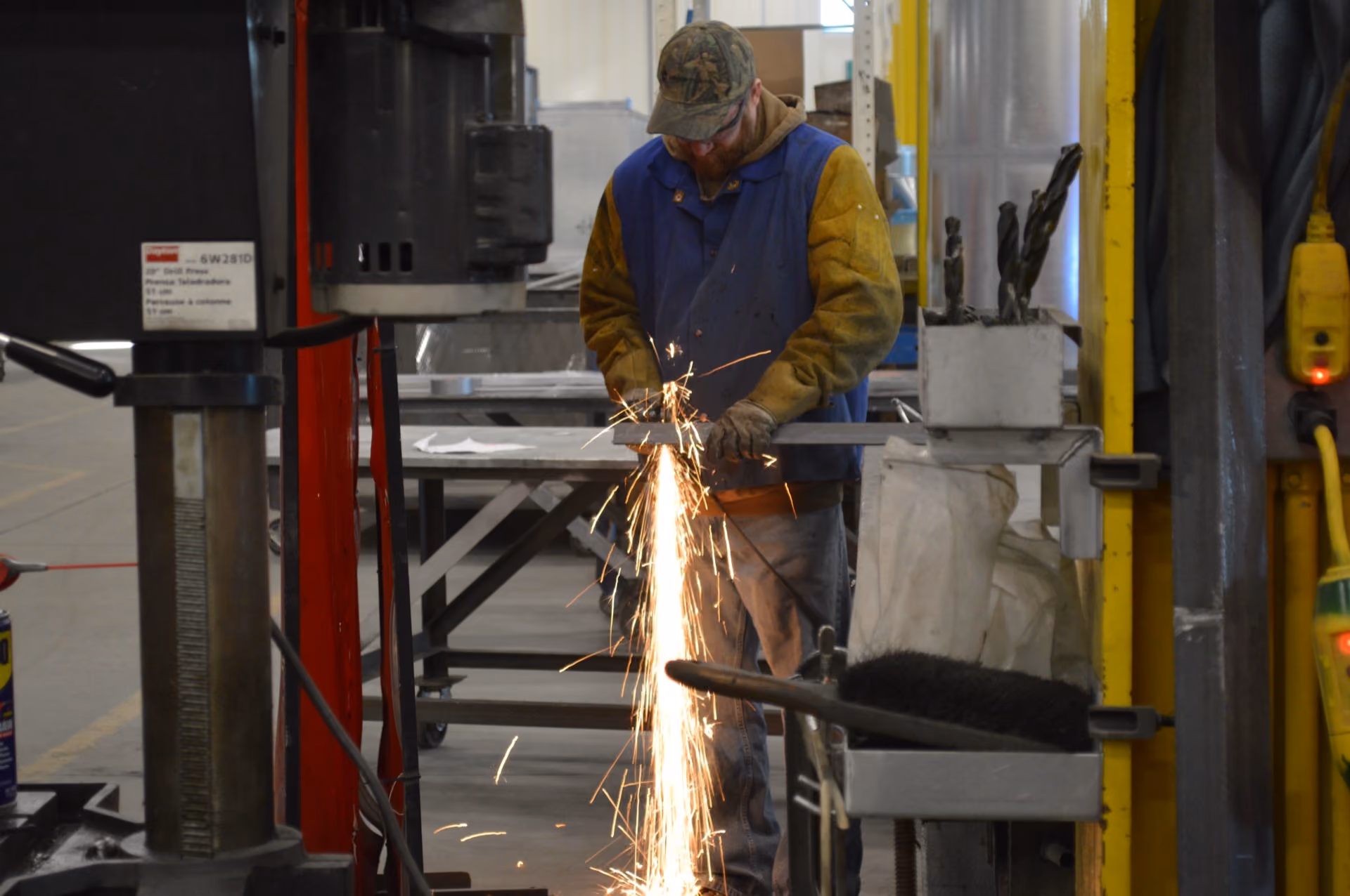 Worker in protective clothing grinding metal with sparks flying in an industrial workshop.