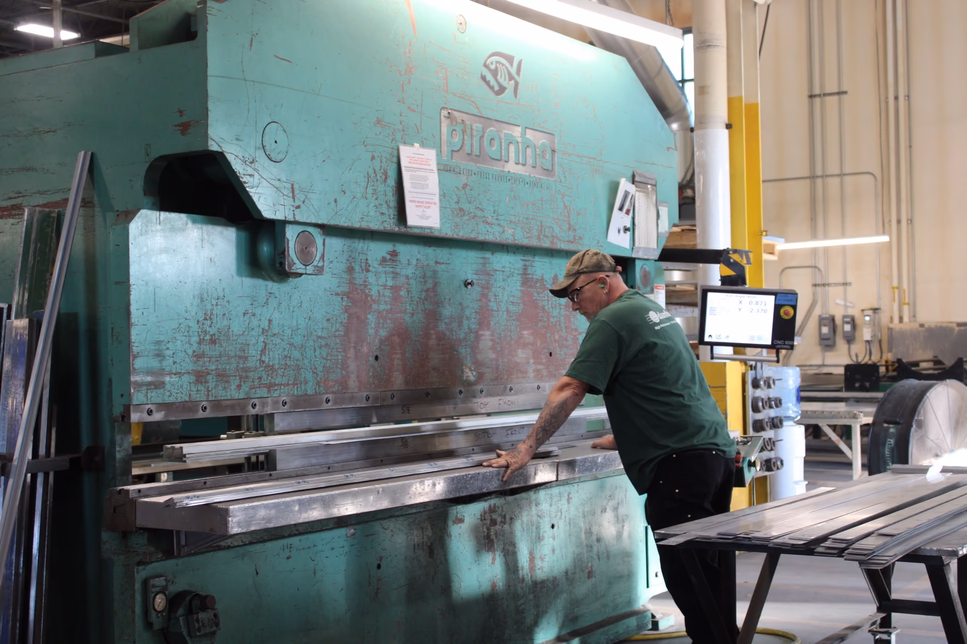 Worker operating large green Piranha metal press machine shaping metal strips in a workshop.