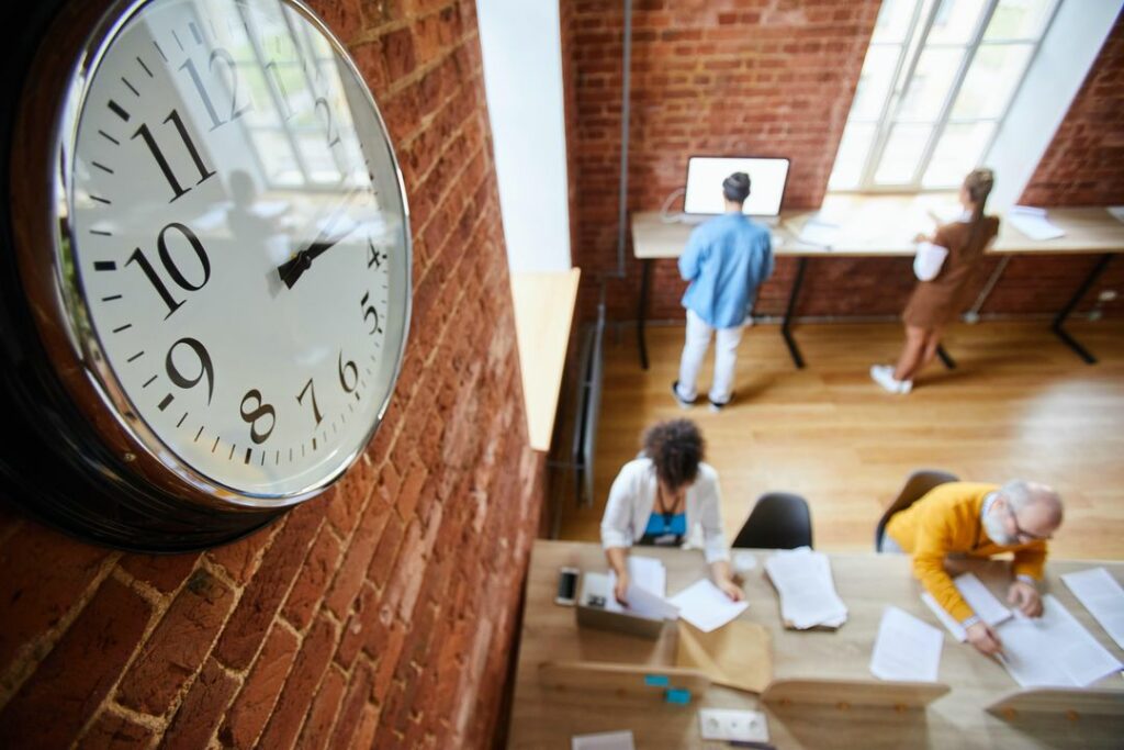 Équipe au travail dans un bureau, avec une grande horloge au premier plan