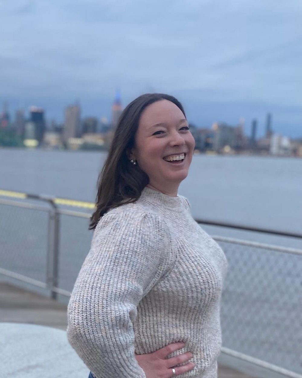 Kelly, smiling, on the waterfront with the Manhattan skyline behind her