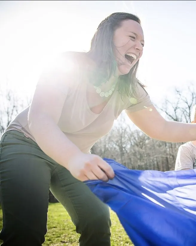 Kelly laughing while playing a parachute game outdoors with a child