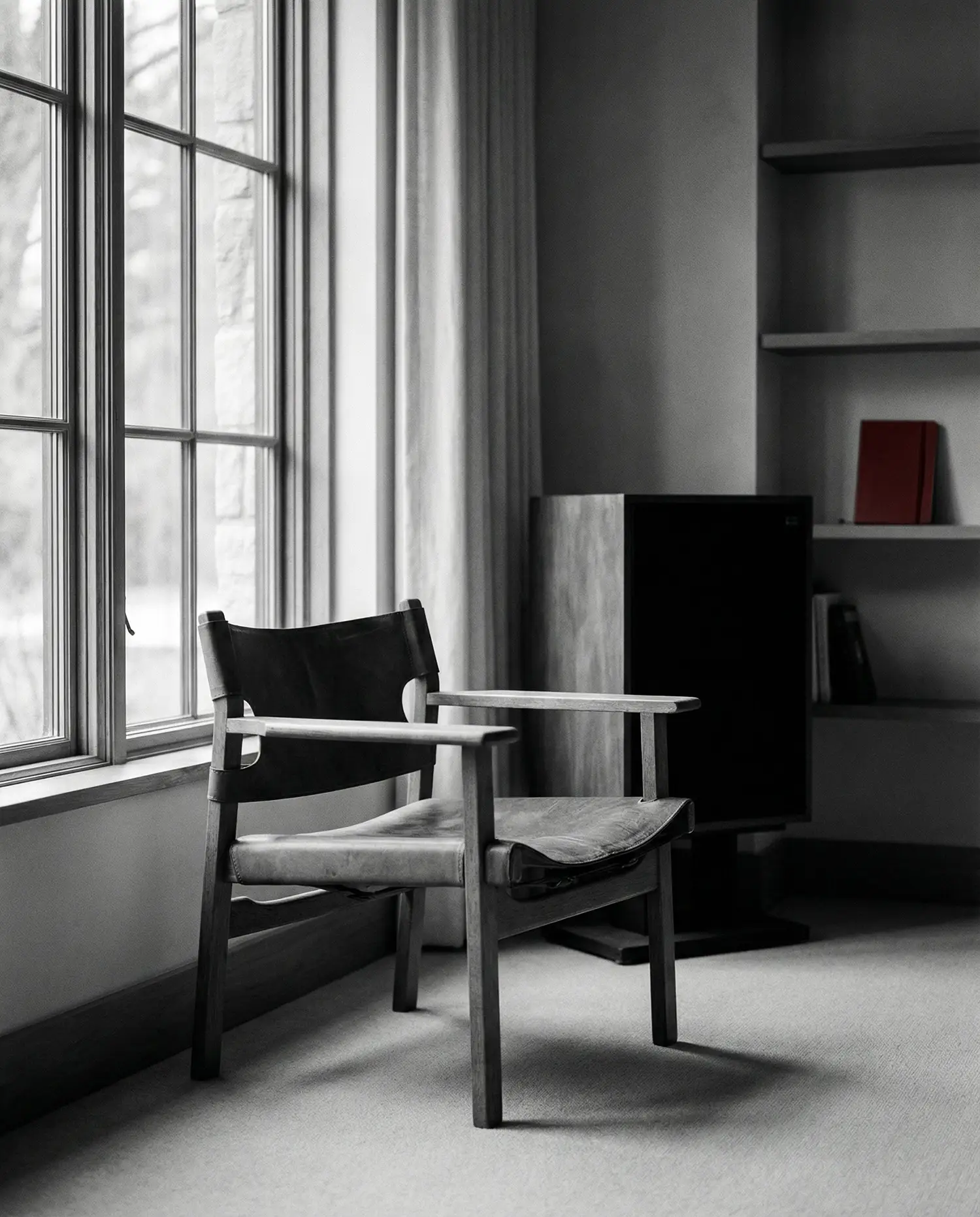 Wooden chair with leather seat and backrest beside a large window in a minimalist room.