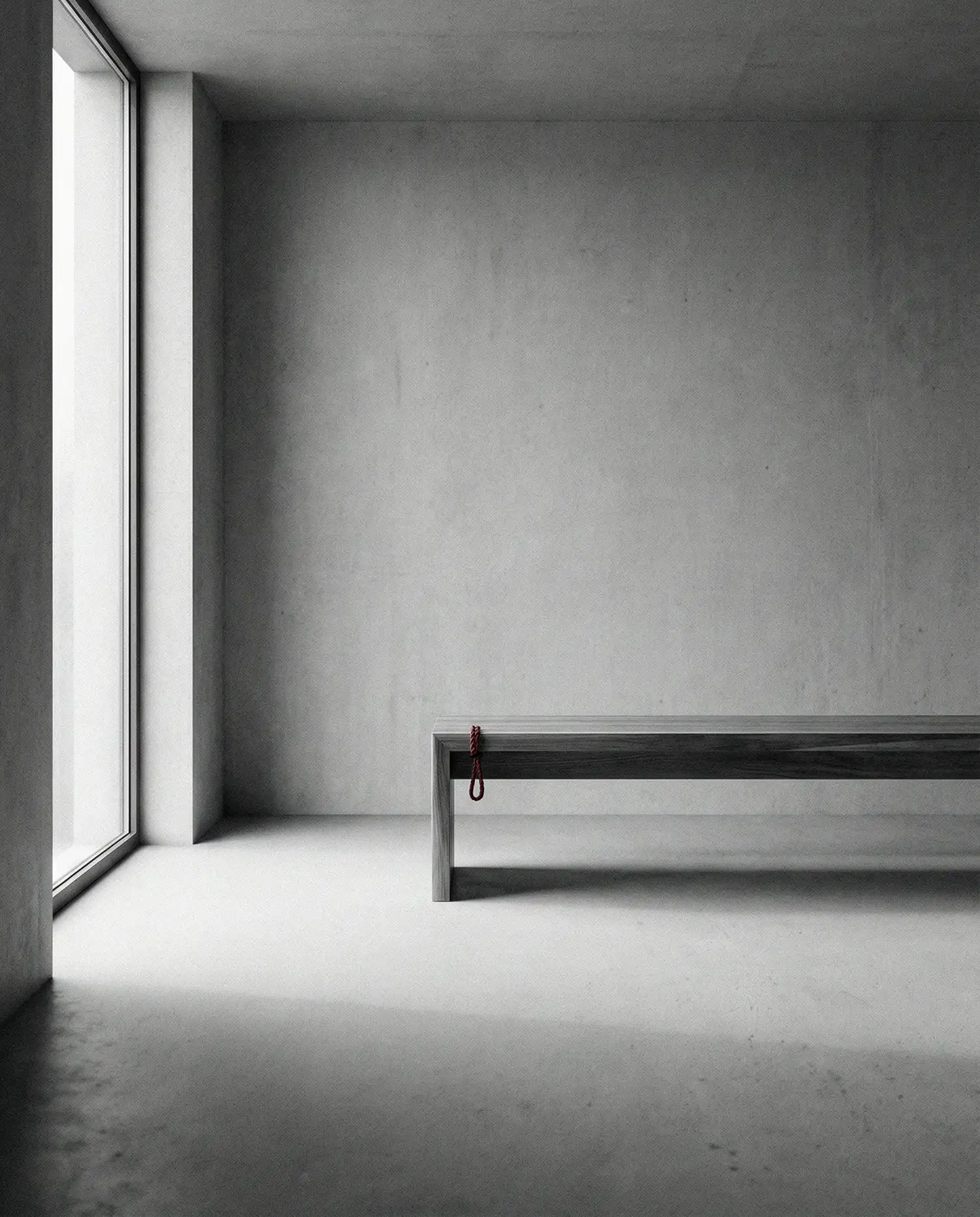 Minimalist empty room with concrete walls, large window, and a wooden bench with a small red rope hanging from its corner.