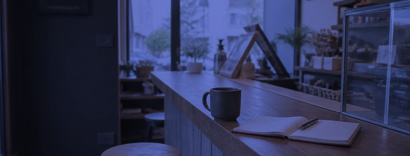 Coffee cup and open notebook on a kitchen counter beside a window.