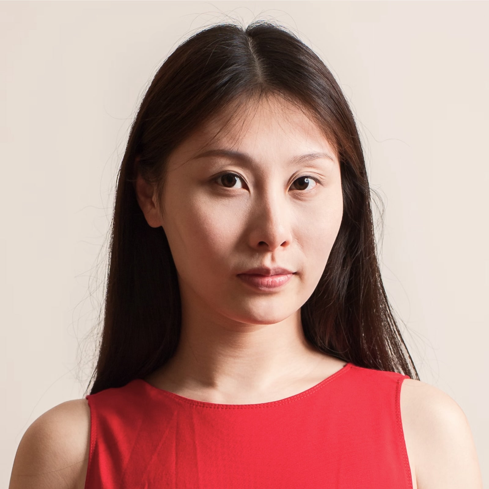 Portrait of a woman with long dark hair wearing a sleeveless red top against a neutral background.