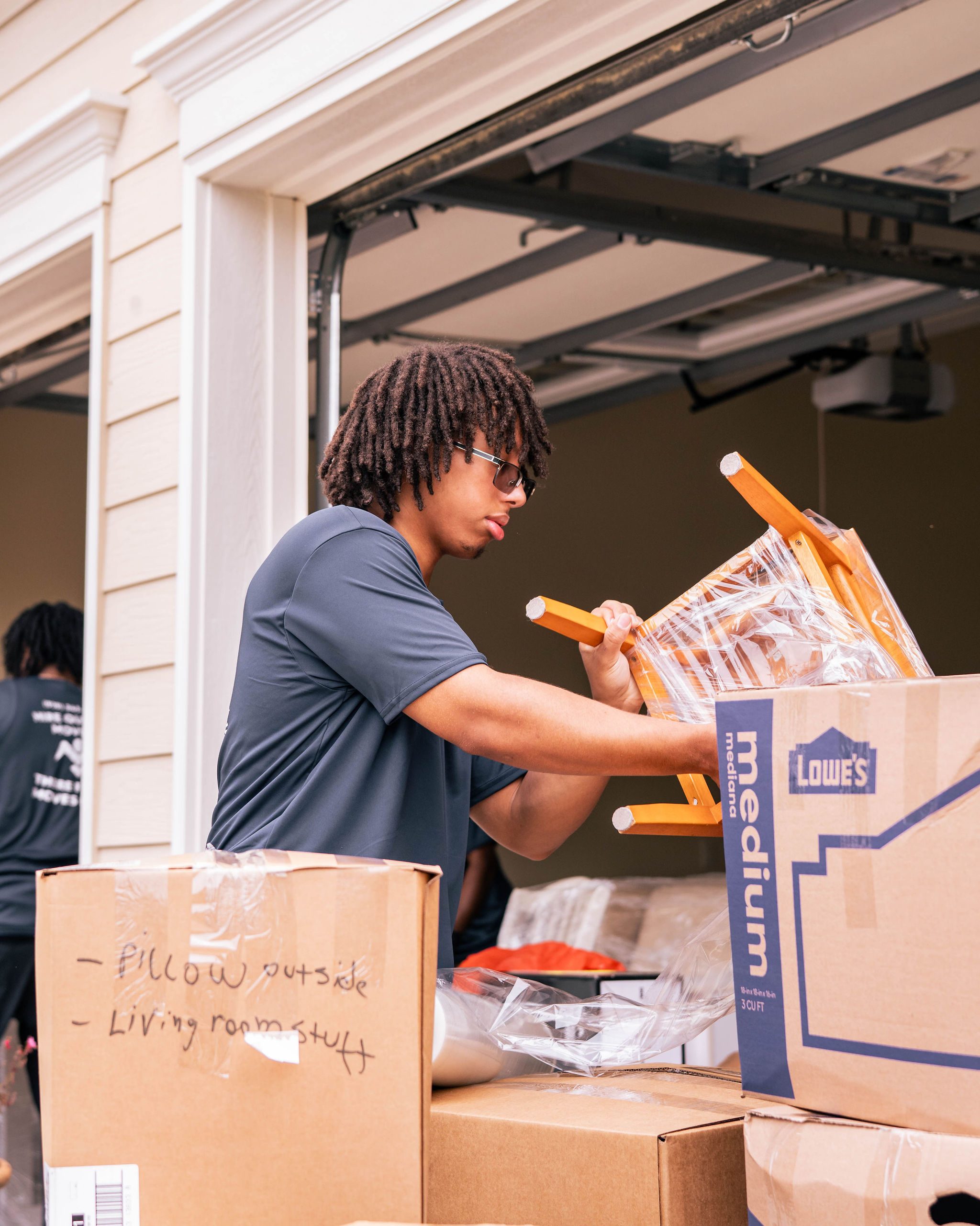 Person packing wooden chair into moving boxes in a garage during a move.