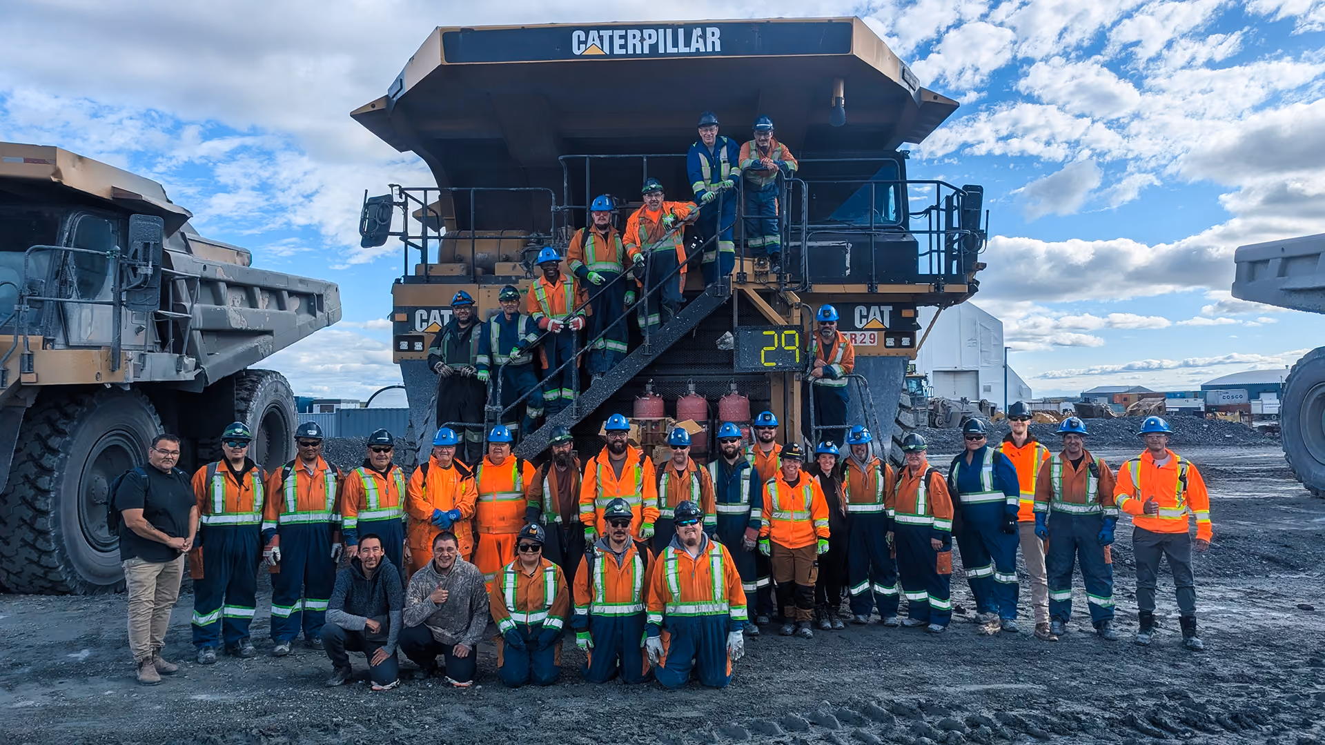 Équipe du Groupe Gilbert réunie devant de la machinerie lourde Caterpillar sur un chantier minier.