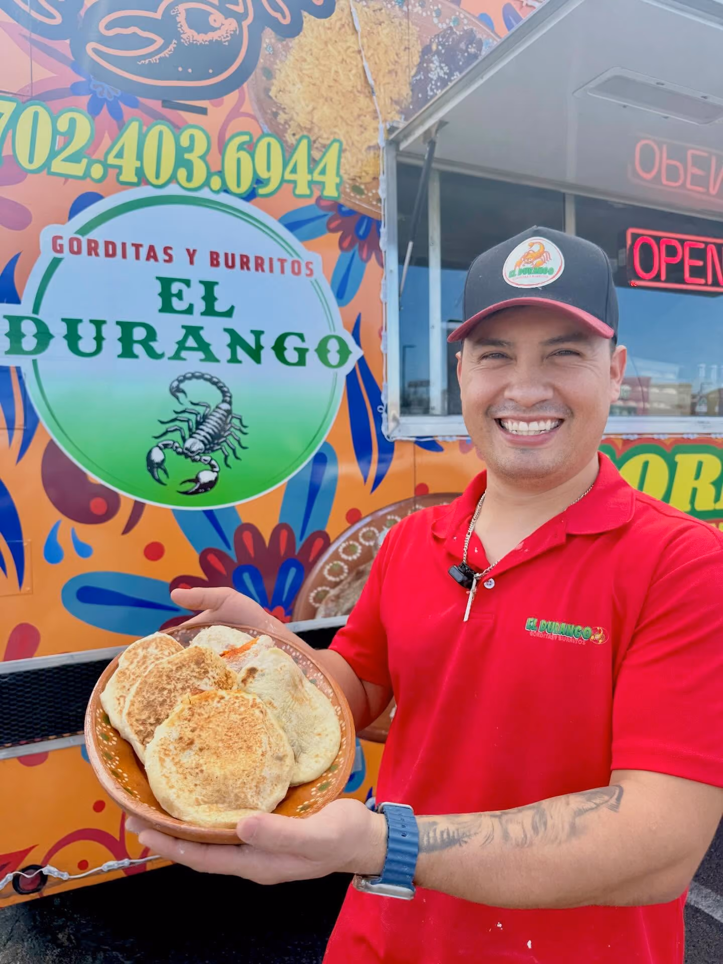 Smiling man in red shirt and cap holding a bowl of gorditas in front of El Durango food truck.