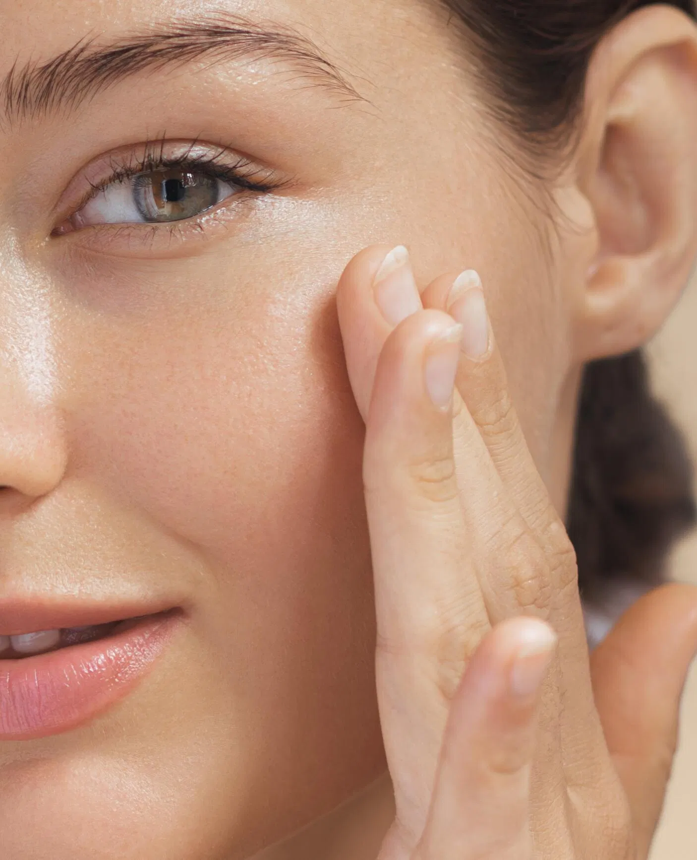 Woman with a radiant complexion gently applying skincare to her cheek