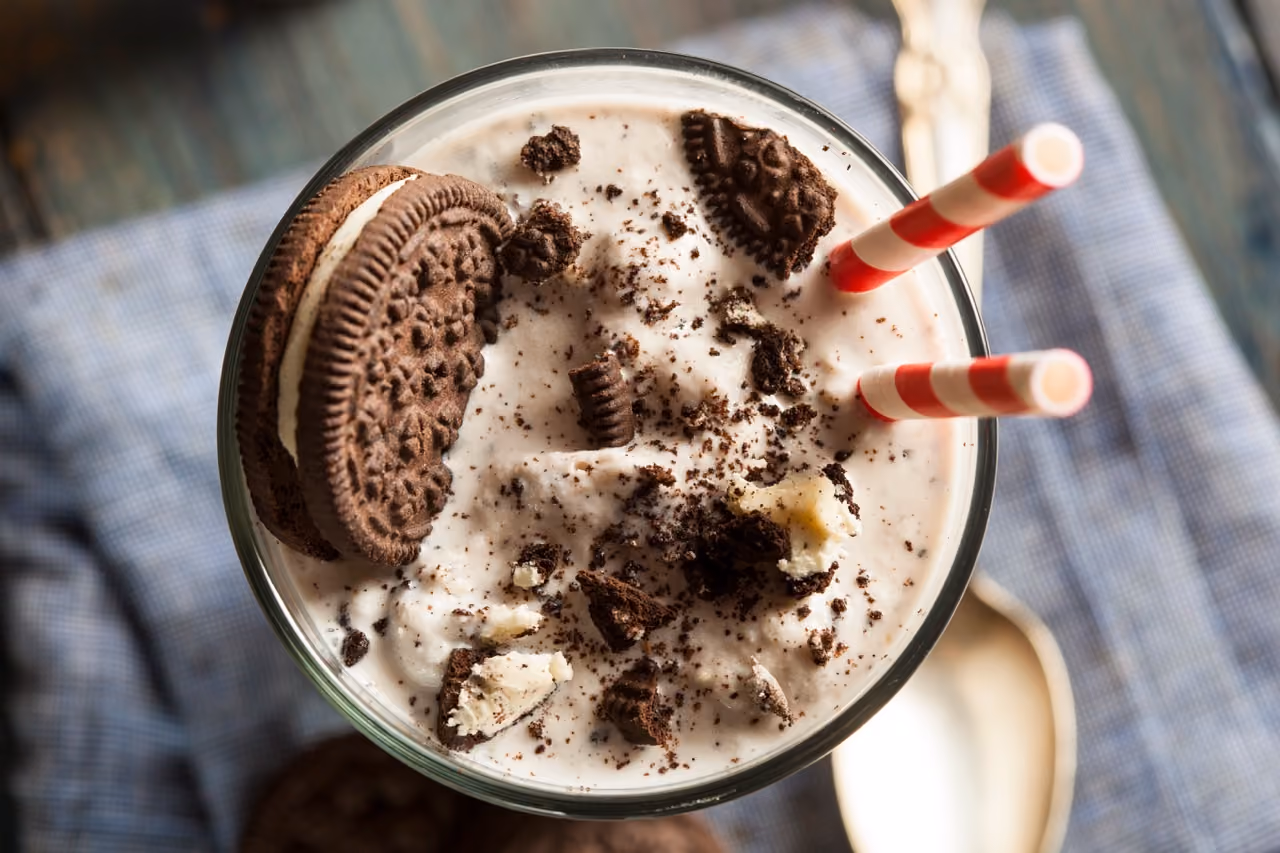 Cookies and cream milkshake topped with cookie crumbs and two red-striped straws in a glass.