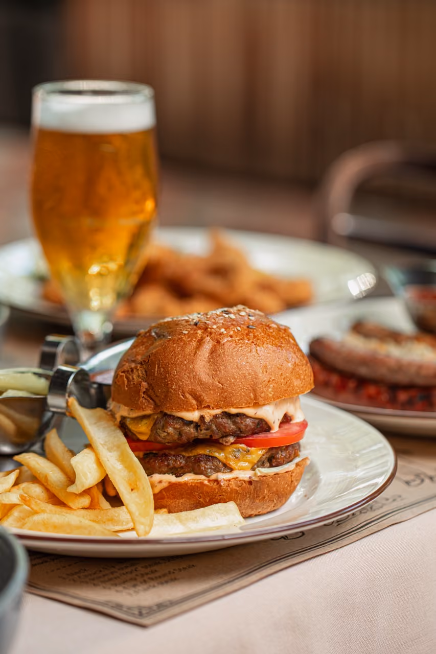 Double cheeseburger with tomato and fries on a plate beside a glass of beer.