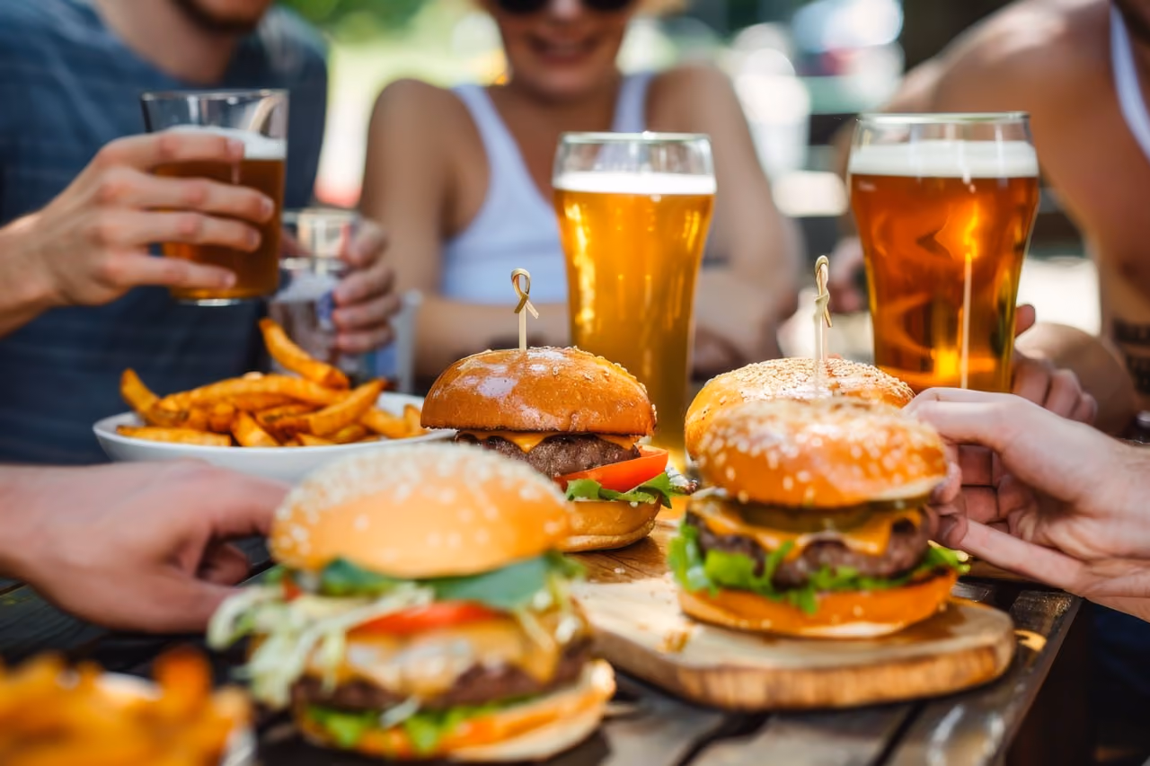 Four people enjoying burgers, fries, and glasses of beer at an outdoor table.