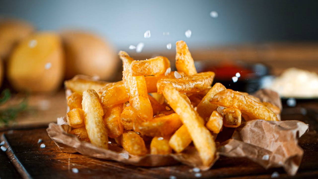 Close-up of crispy golden French fries with coarse salt sprinkled on and around them.