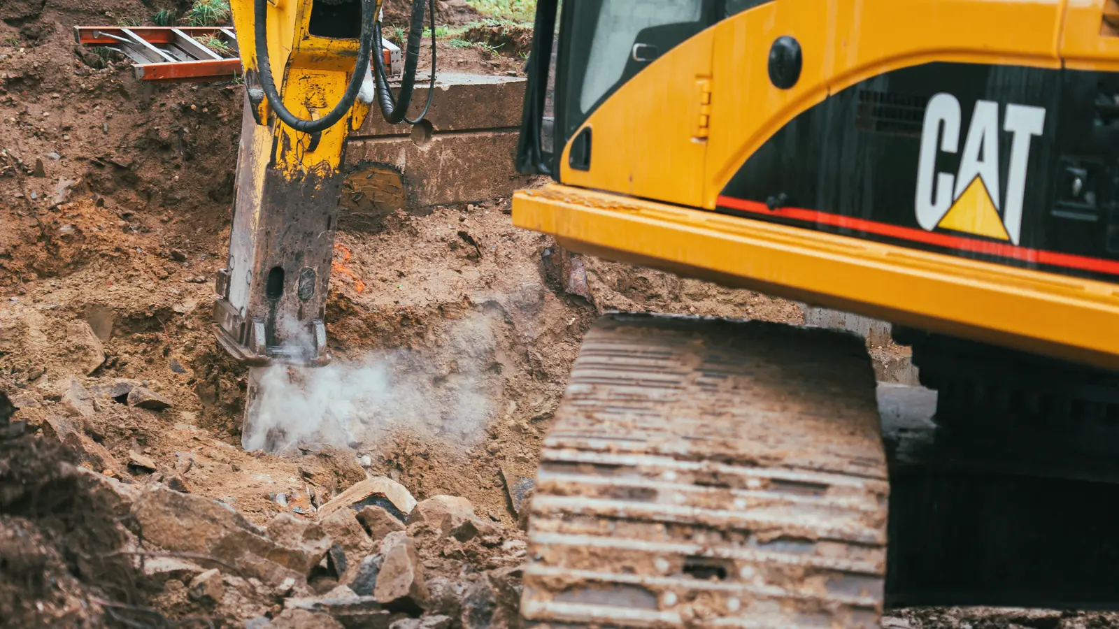 Excavator-mounted breaker removing rock in a working excavation.