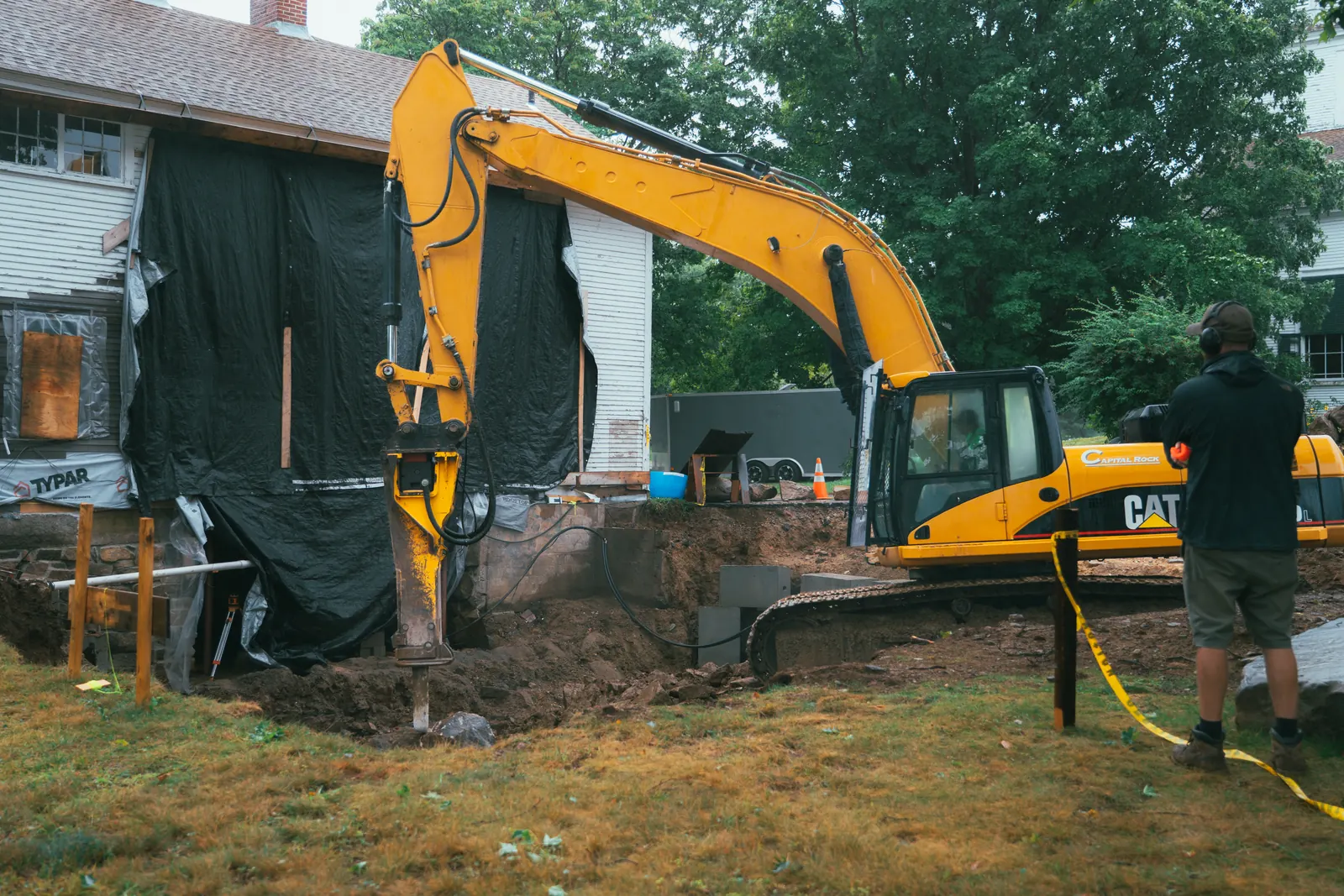 Excavator with a hydraulic breaker working beside a house