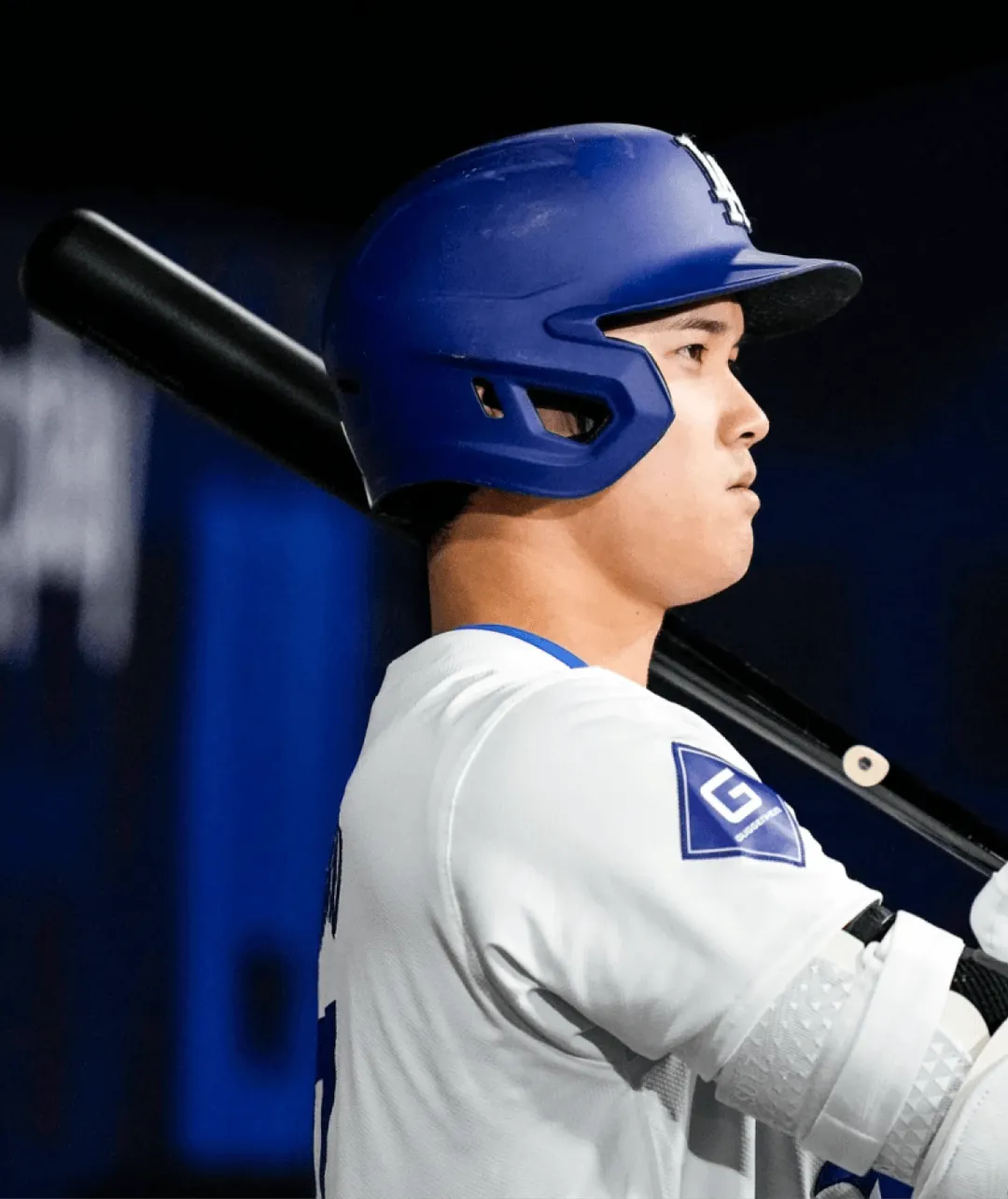 Baseball player wearing a blue helmet and white uniform holding a bat over his shoulder, looking focused.