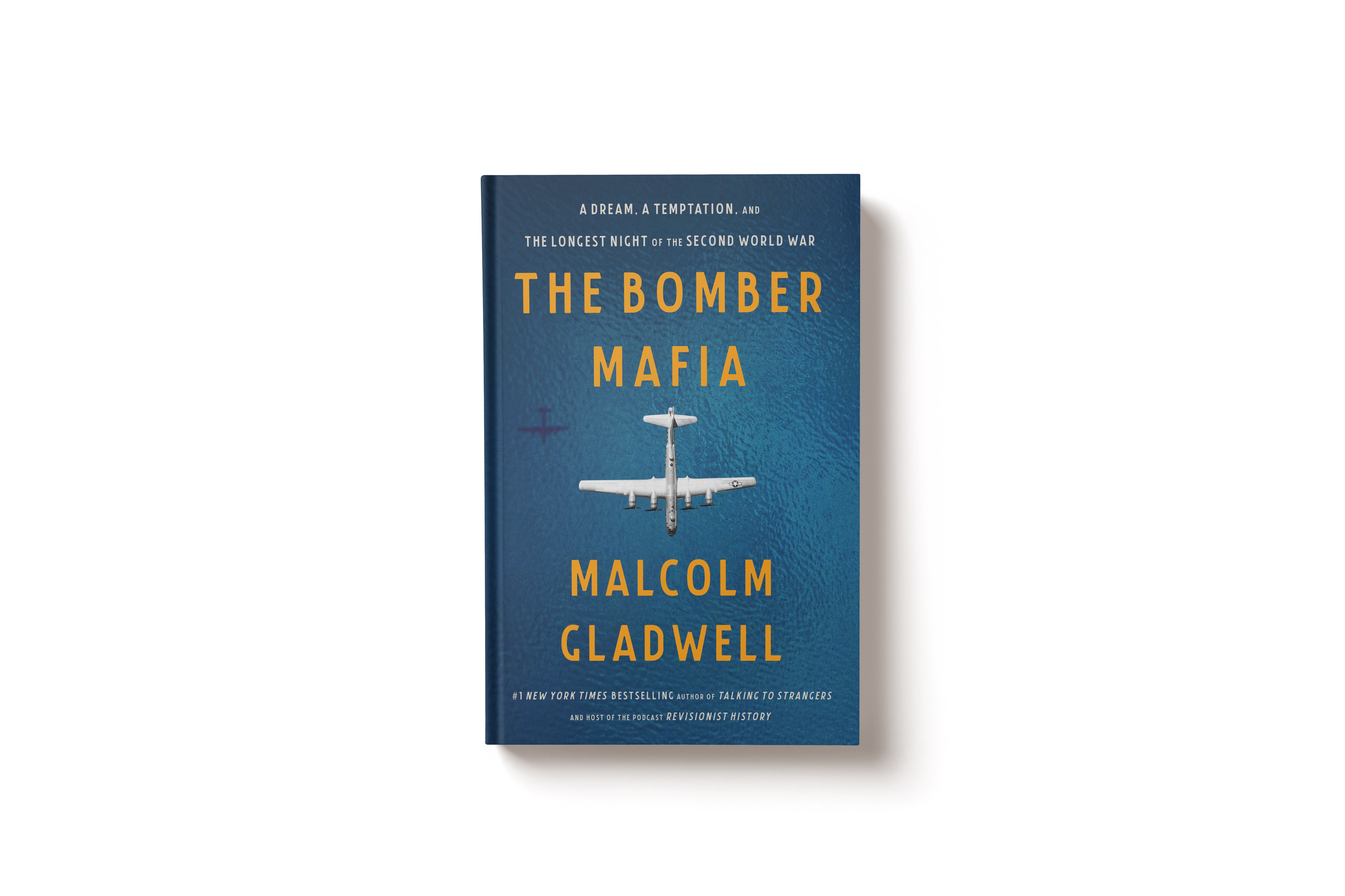 Hardcover book titled 'The Bomber Mafia' by Malcolm Gladwell with text about a dream, temptation, and the longest night of the Second World War, featuring an aerial image of a bomber plane over blue water.