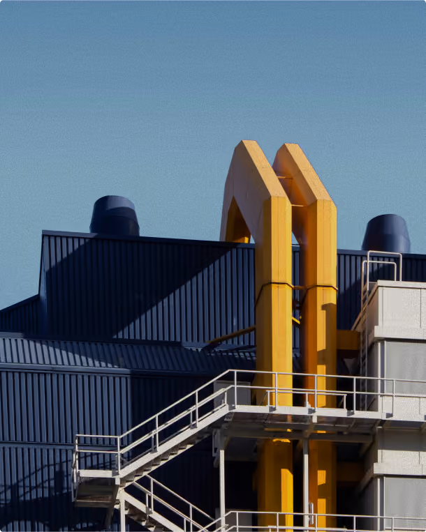 Industrial building with blue corrugated walls, yellow pipes, and metal staircases against a clear sky.
