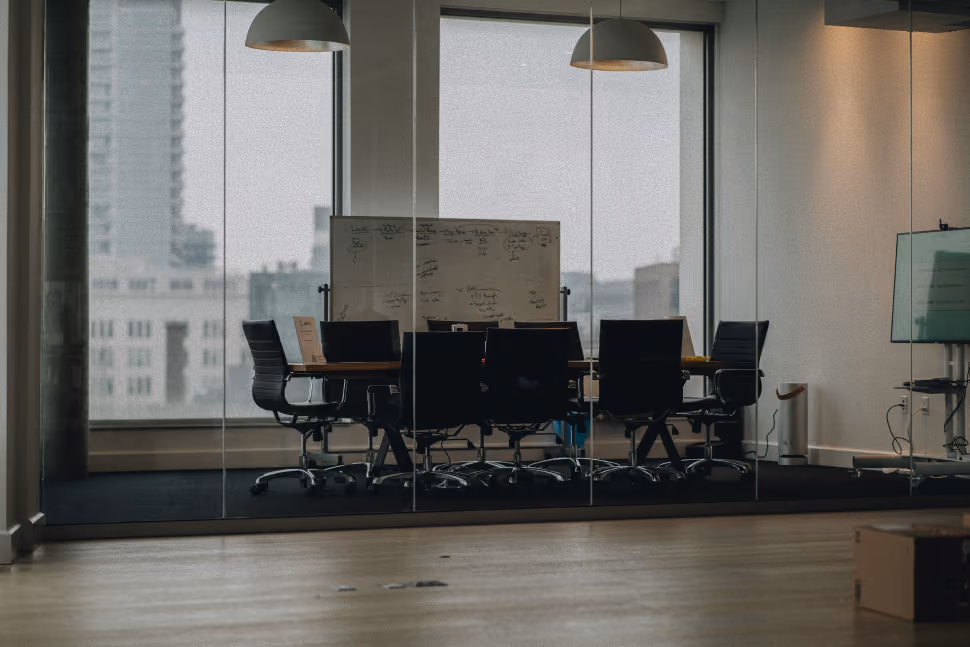 Empty modern conference room with black chairs, a whiteboard, and large windows overlooking buildings.