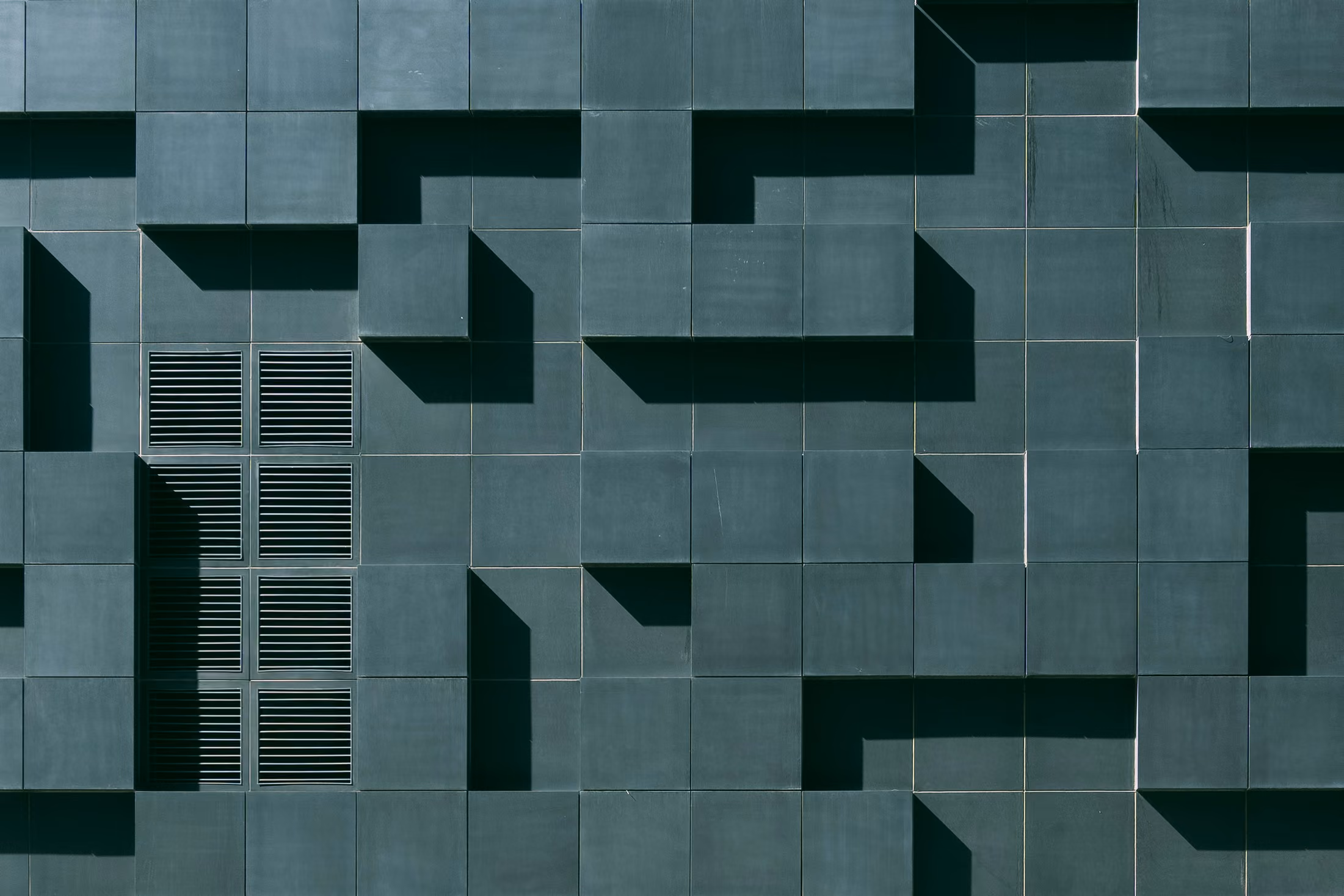 Pattern of dark square wall panels with some protruding to form shadows and a side vent.