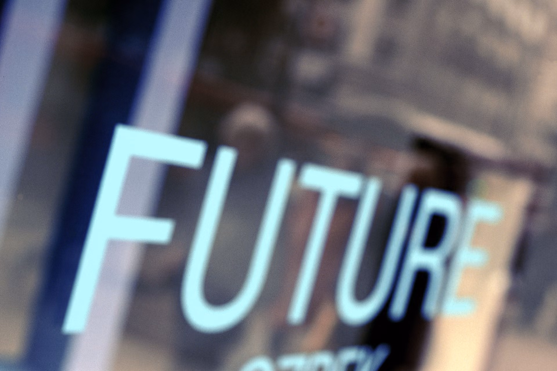 The word FUTURE in large blue letters on a glass surface with blurred background figures.