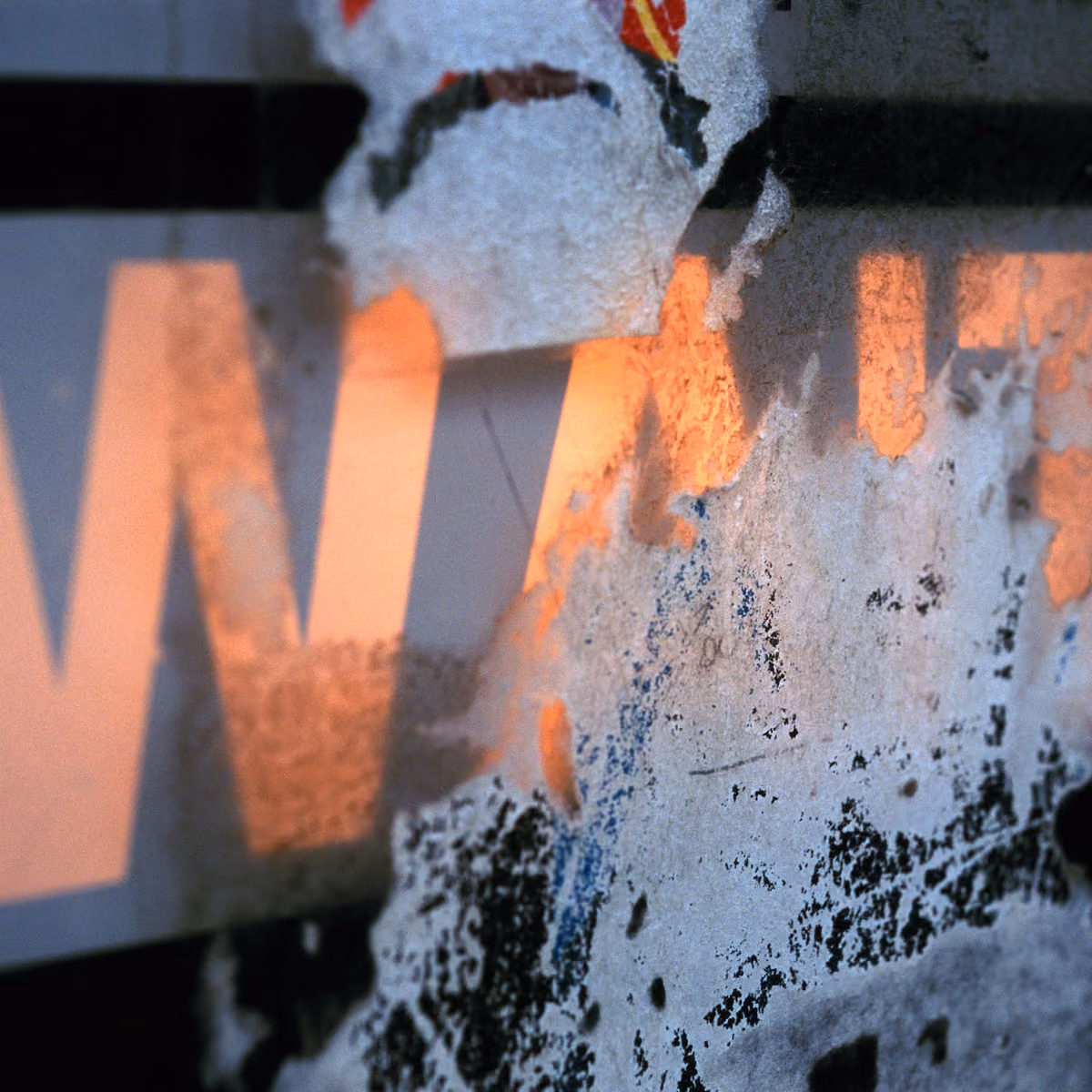 Peeling paint on a textured surface partially revealing orange letters in the background.