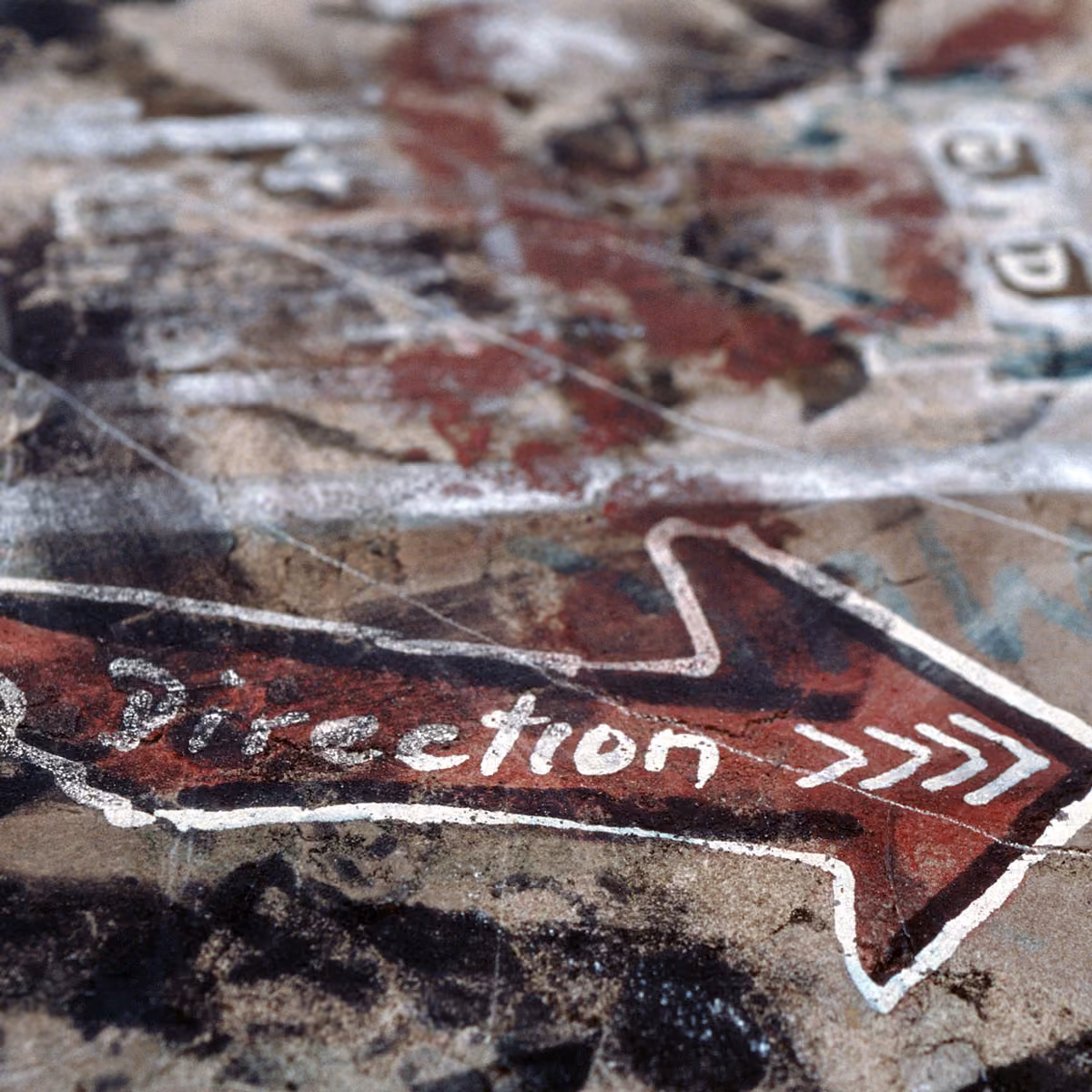 Red arrow painted on rough surface with the word 'Direction' and three white arrow marks.