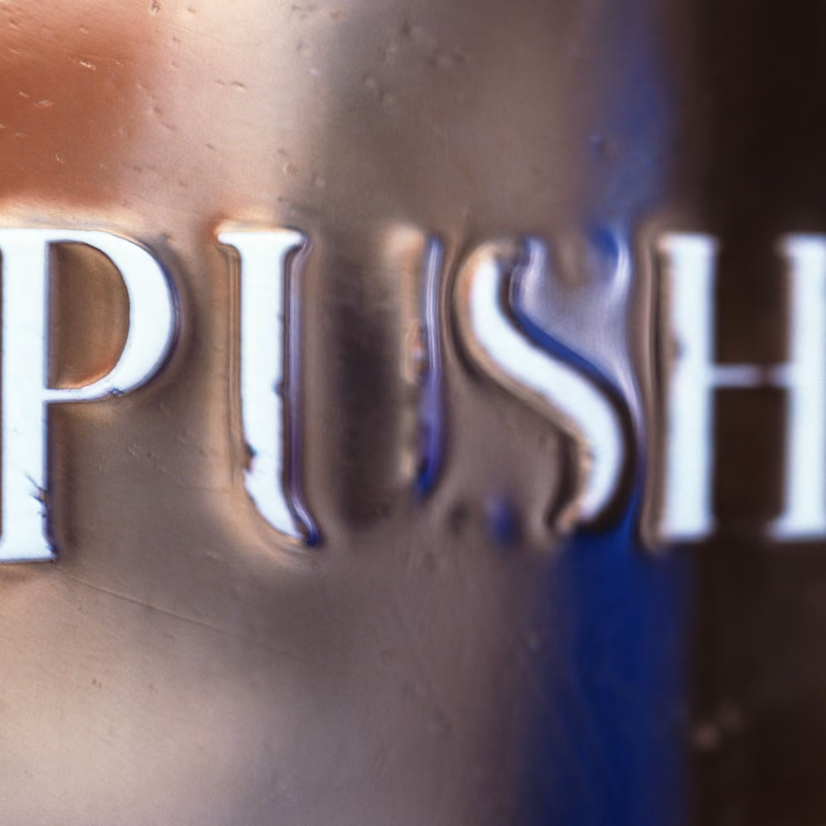 Close-up of frosted glass with white embossed letters spelling 'PUSH'.