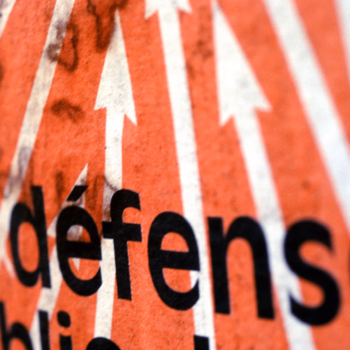 Close-up of word 'defense' in black on orange background with white upward arrows.