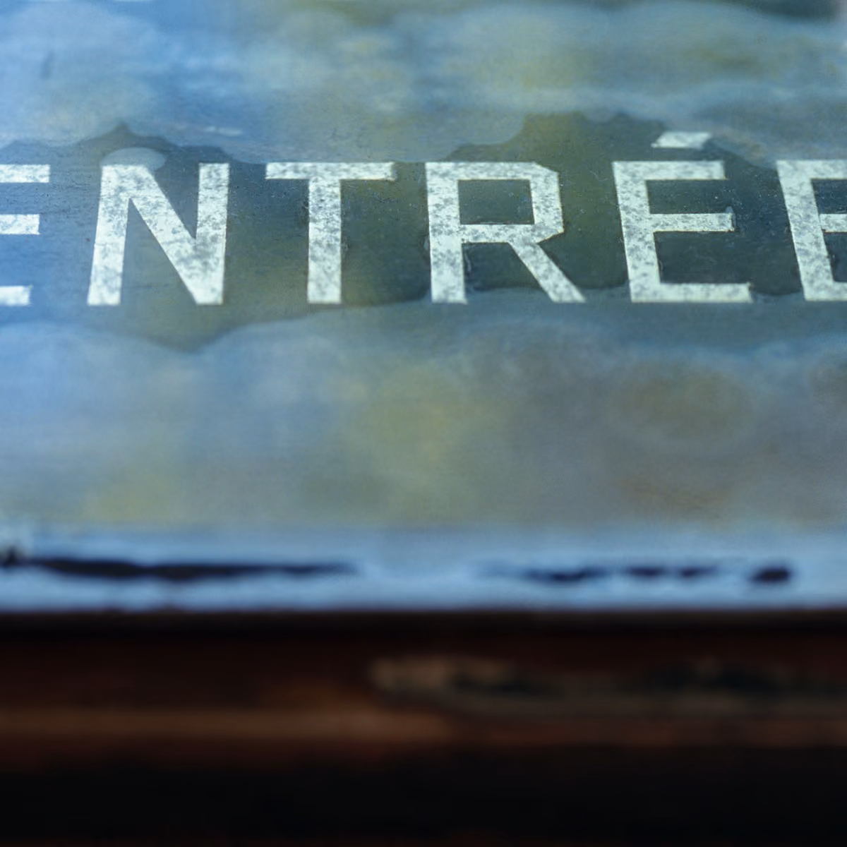 Close-up of white text reading "ENTRÉE" on a textured surface with water stains.