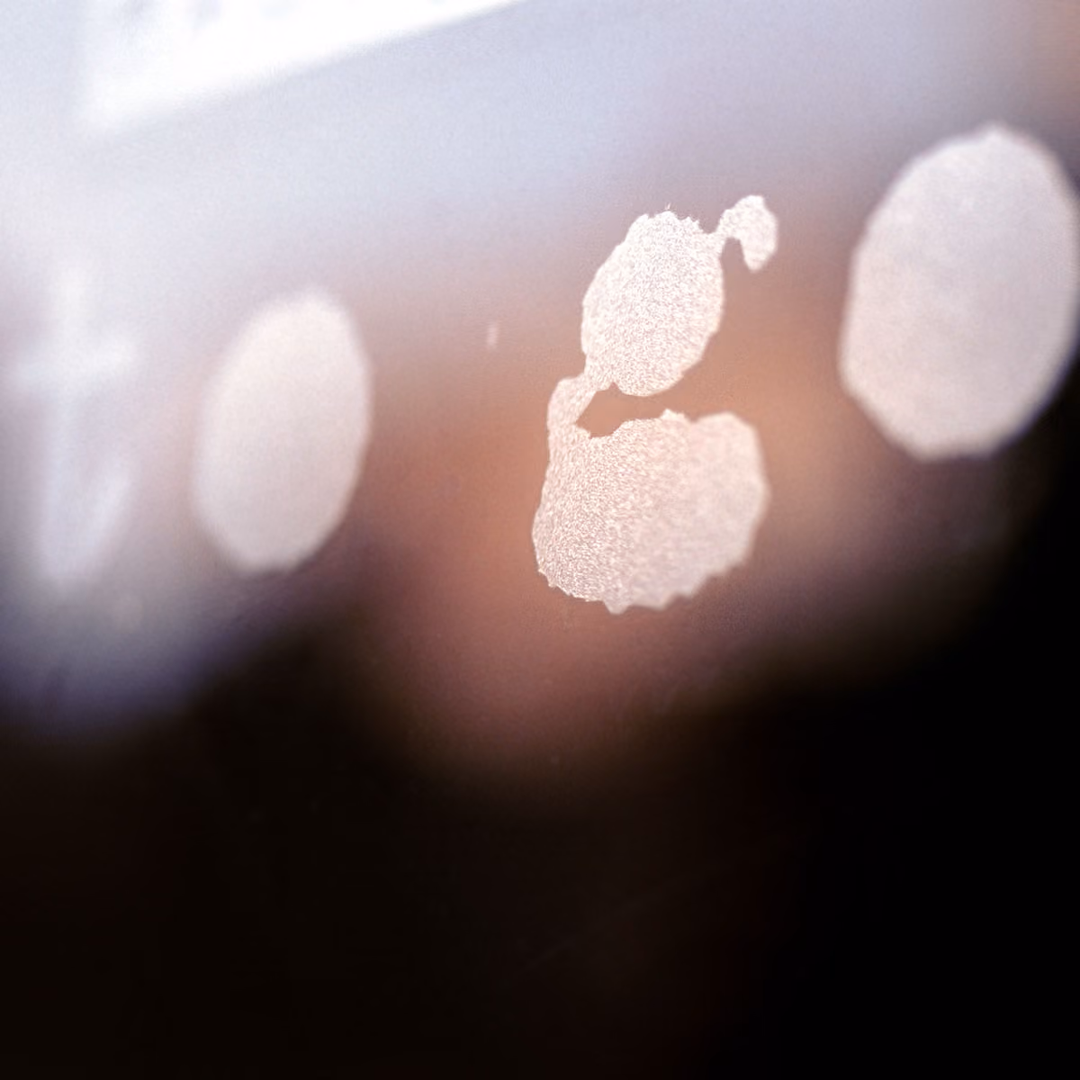 Close-up of frosted glass with circular and irregular white patterns on a blurred background.
