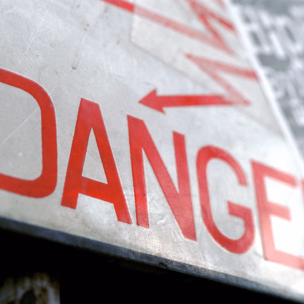 Close-up of a weathered metal sign with red text spelling DANGER and an arrow pointing left.