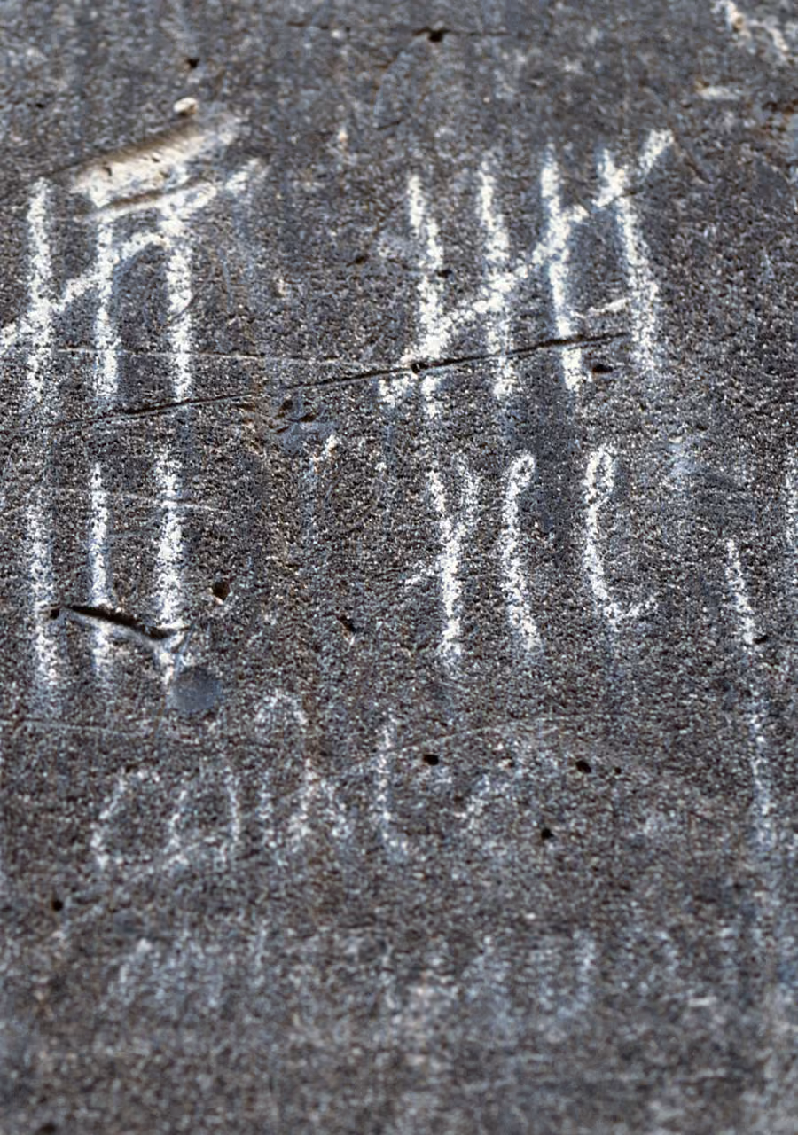 White chalk tally marks and illegible writing on rough black asphalt surface.