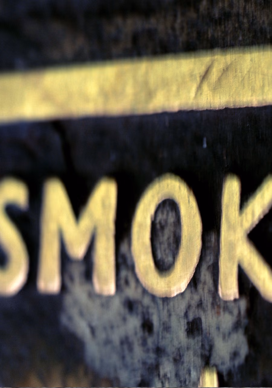 Close-up of the word 'SMOKE' in yellow letters on a dark textured background.