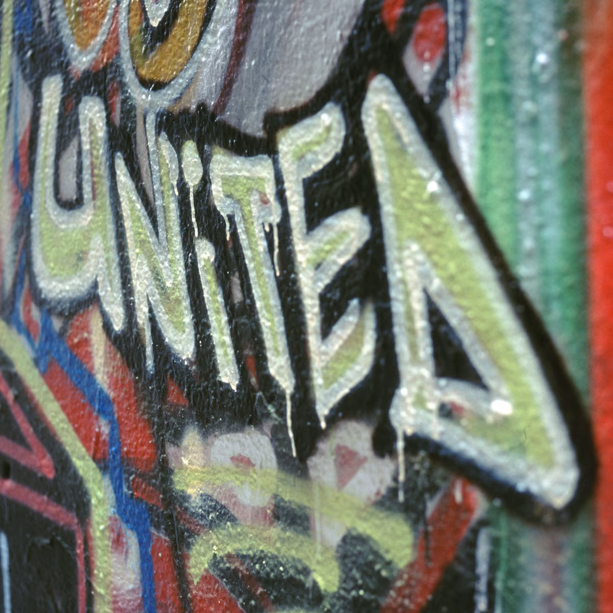 Close-up of graffiti art with the word UNITED painted in large white and green letters on a textured wall.