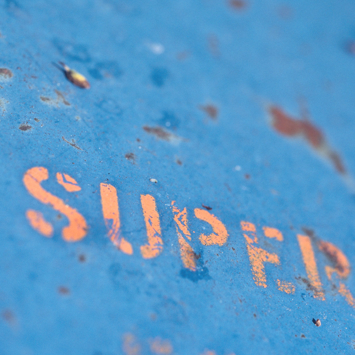 Close-up of faded orange text spelling 'SUPER' on a worn blue metal surface.