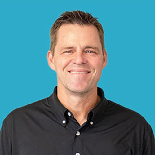Smiling man, Donny R.,  with short brown hair wearing a black button-up shirt against a blue background.