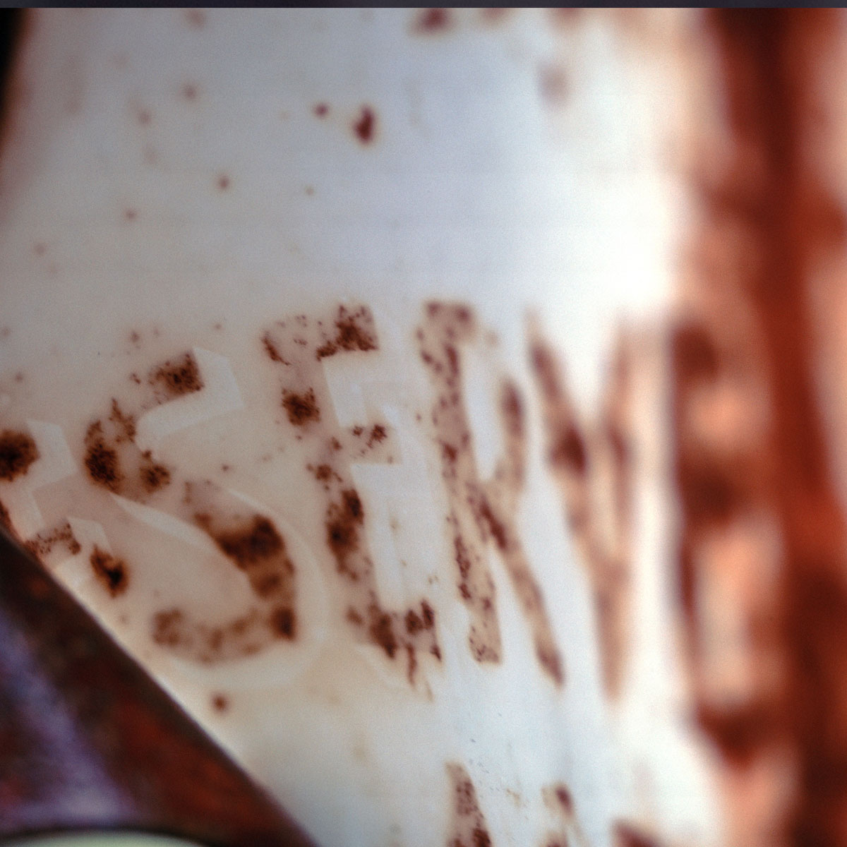 Rusty blue metal surface with worn orange letters partially spelling 'SUPER'.